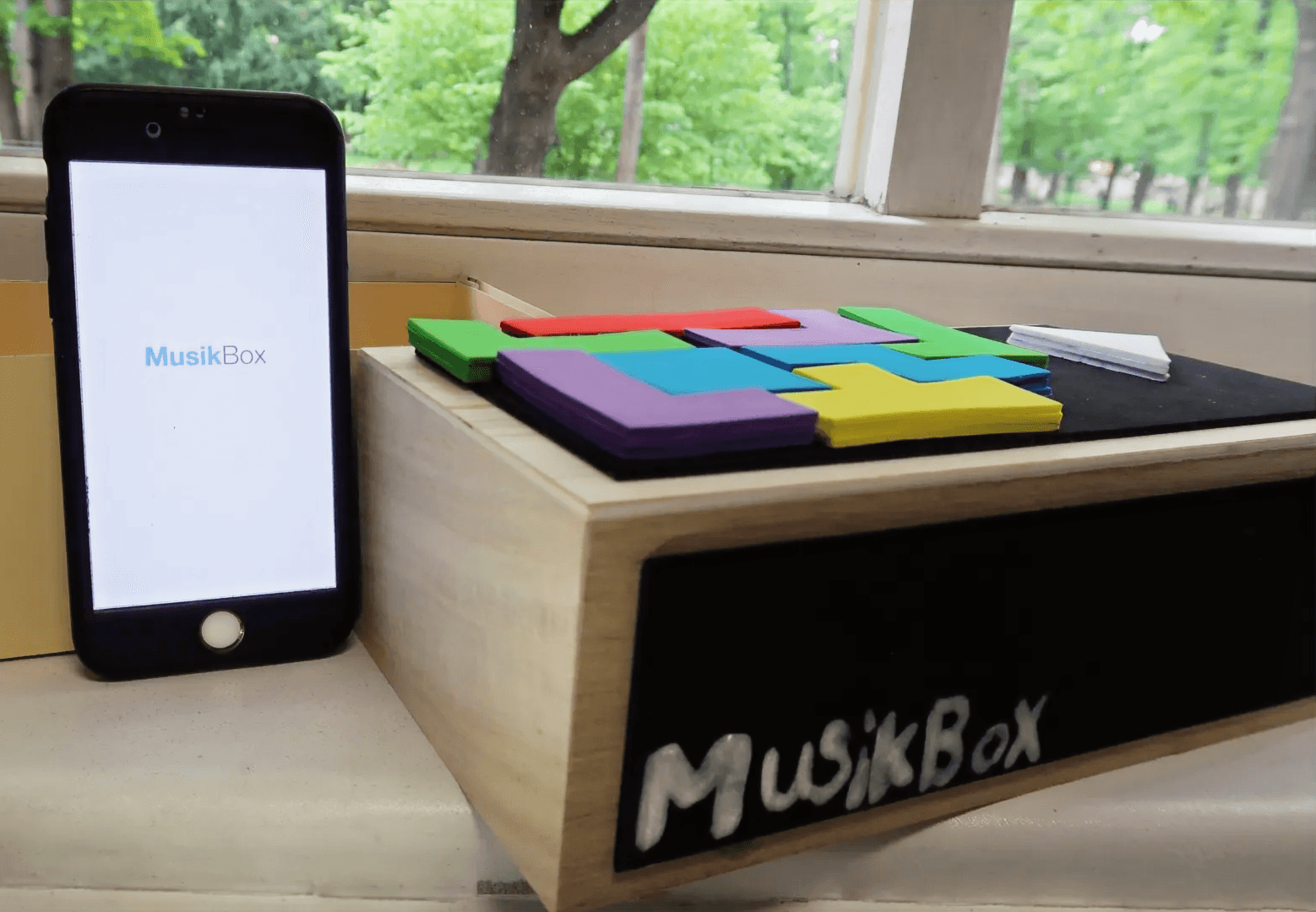 The MusikBox app on a phone next to the speaker with its coloured Tetris blocks
