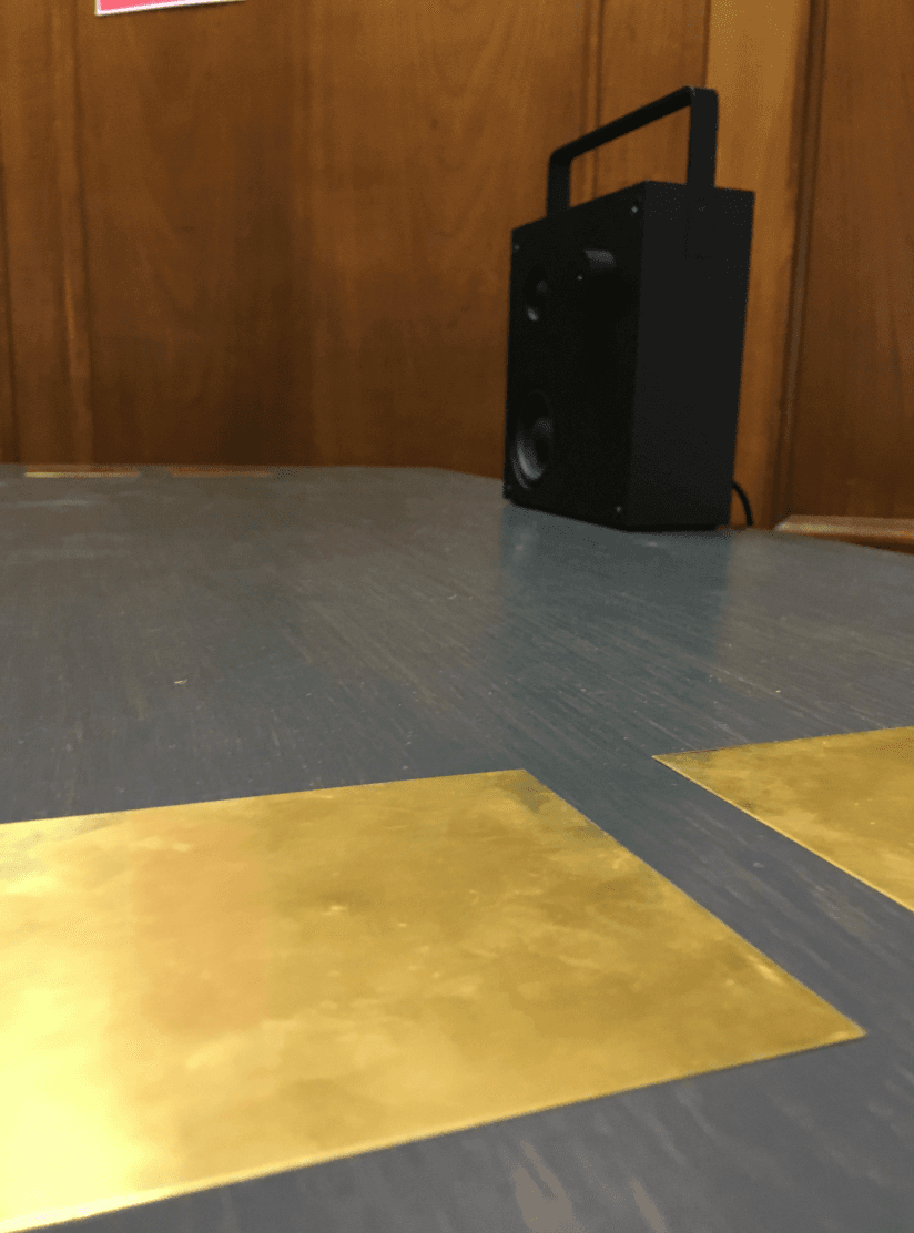 Close-up of the brass plates on the table surface with the speaker behind