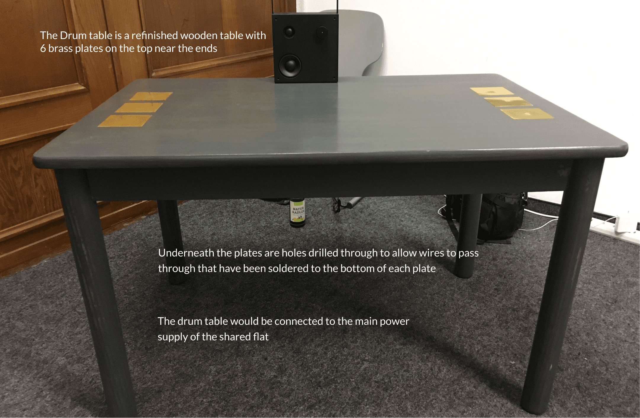 Annotated drum table: a refinished wooden table with 6 brass plates, wires soldered beneath each plate through drilled holes, connected to the flat's main power supply